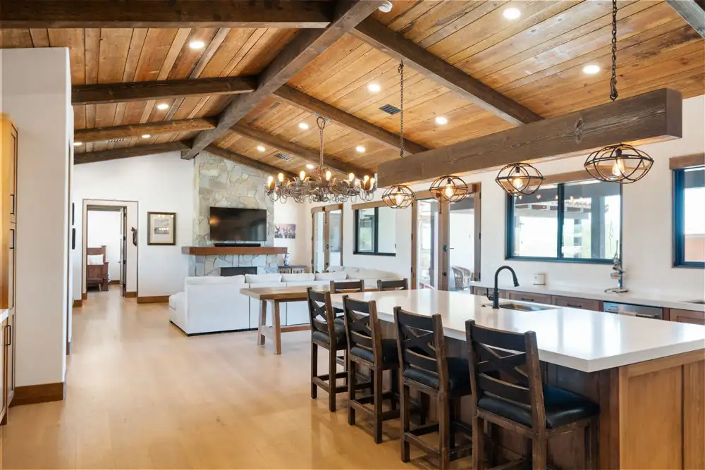 Open concept kitchen and living room with wood plank ceiling, exposed box beams, stone accent wall, modern farmhouse interior